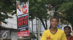 Dua Karyawan toko melintasi benner ilklan beli rumah dapat istri di kawasan Nonongan, Solo (3/2/2016). Iklan di pasang untuk menarik minat calon pembeli. (Liputan6.com/Boy Harjanto)