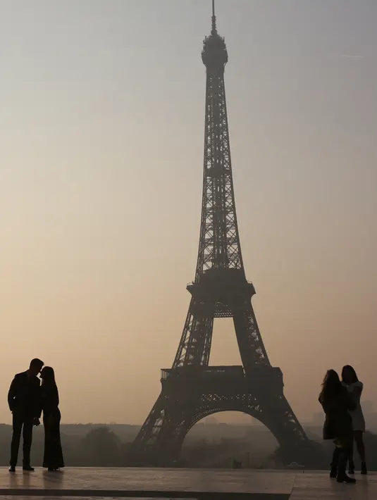 Sejumlah wisatawan saat menikmati matahari terbit di dekat menara Eiffel, Paris (11/3/2016). (AFP/Ludovic MARIN)