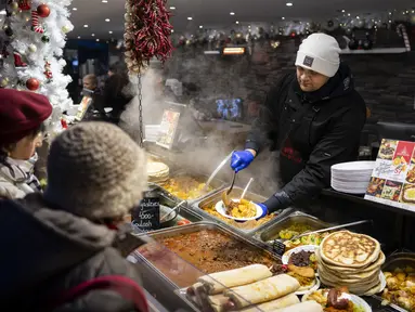 Seorang pekerja melayani pelanggan di pasar Advent Bazilika, salah satu pasar Natal luar ruangan paling terkenal di Eropa di pusat kota Budapest, Hungaria, Sabtu, 9 Desember 2023. (AP Photo/Denes Erdos)