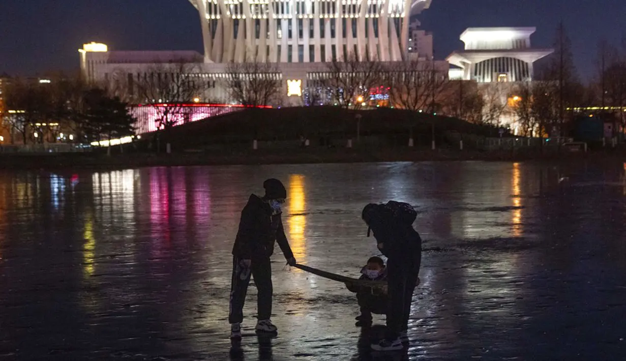 Warga menarik seorang anak melintasi danau beku dekat Olympics Green di Beijing, China, 3 Januari 2022. Libur Tahun Baru dimanfaatkan warga untuk bermain ice skating di sungai dan danau yang membeku. (AP Photo/Ng Han Guan)