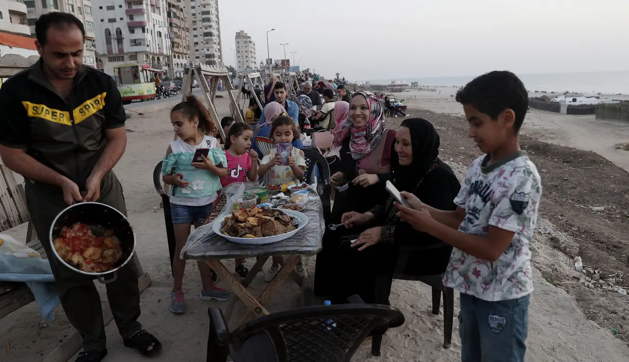 Anggota keluarga menyiapkan makanan mereka sambil menunggu berbuka puasa saat bulan suci Ramadan di pantai Kota Gaza, Palestina, Kamis (21/5/2020). Di tengah pandemi COVID-19, berbuka puasa bersama di pantai Kota Gaza tetap ramai. (AP Photo/Adel Hana)