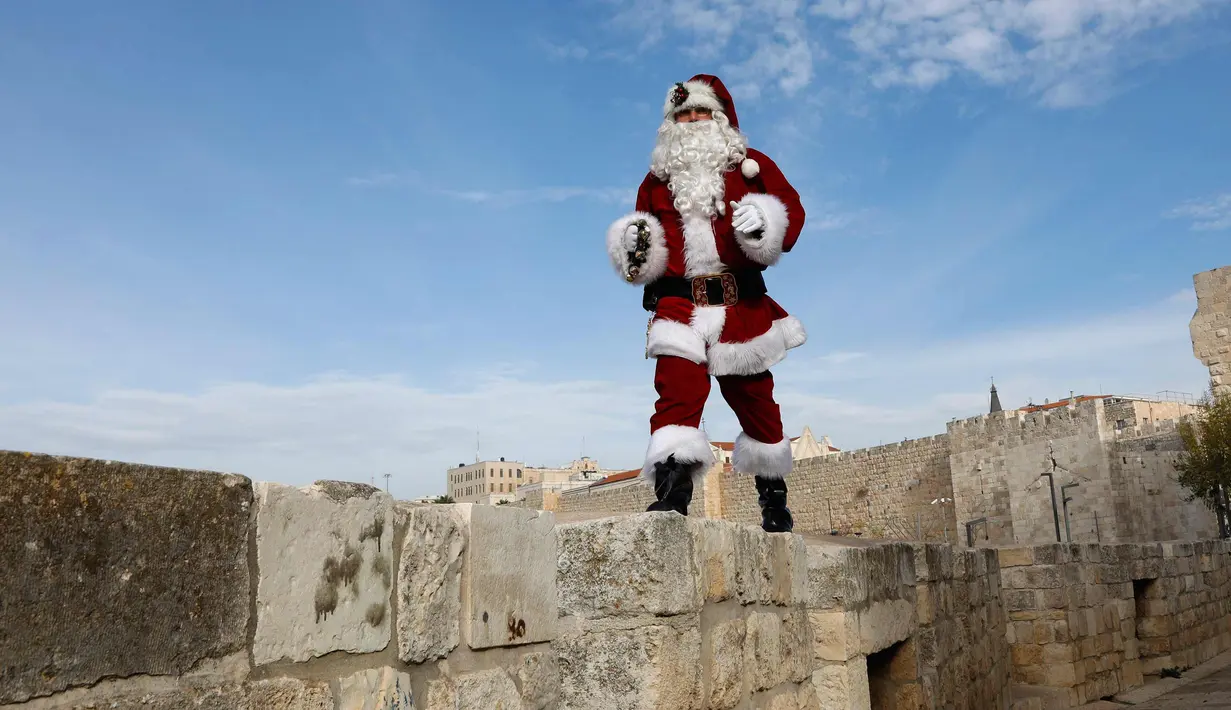 Seorang pria berpakaian seperti Santa Claus berjalan di sepanjang tembok Ottoman Kota Tua Yerusalem (21/12). (AFP Photo/Gali Tibbon)