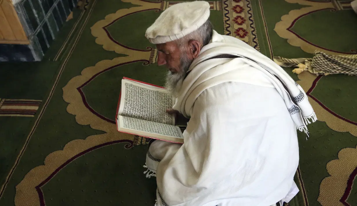 Seorang pria muslim membaca Al-Quran selama melaksanakan salat berjemaah pada hari pertama bulan Ramadan di sebuah masjid di Kabul, Afghanistan, Jumat (24/4/2020). Mereka melaksanakan salat di tengah kekhawatiran akan penularan virus corona COVID-19. (AP Photo/Rahmat Gul)