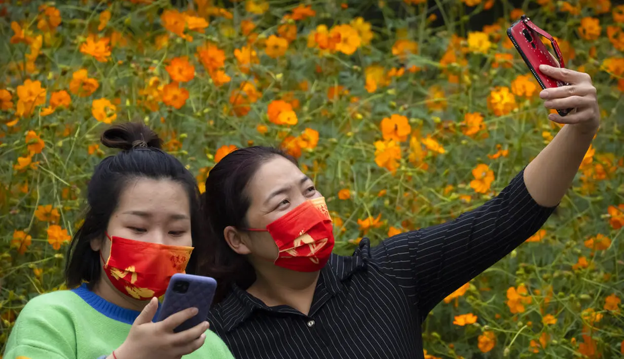 Seorang wanita mengenakan masker bertuliskan "I love you China" berpose untuk selfie dengan bunga mekar di taman umum di Beijing, Sabtu (2/10/2021). Pengunjung memadati taman dan lokasi wisata di Beijing saat China merayakan hari kedua masa libur Hari Nasional. (AP Photo/Mark Schiefelbein)
