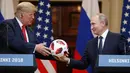 Presiden Rusia Vladimir Putin memberikan bola Piala Dunia 2018 kepada Presiden Amerika Serikat, Donald Trump selama konferensi pers bersama usai pertemuan mereka di Istana Presiden di Helsinki, Finlandia, Senin (16/7). (AP/Alexander Zemlianichenko)