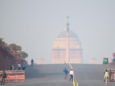 Orang-orang berjalan di dekat istana kepresidenan di tengah kondisi kabut asap tebal di New Delhi (15/11/2021). Otoritas kota New Delhi tengah mempertimbangkan penguncian wilayah akibat kian memburuknya polusi udara. (AFP/Money Sharma)