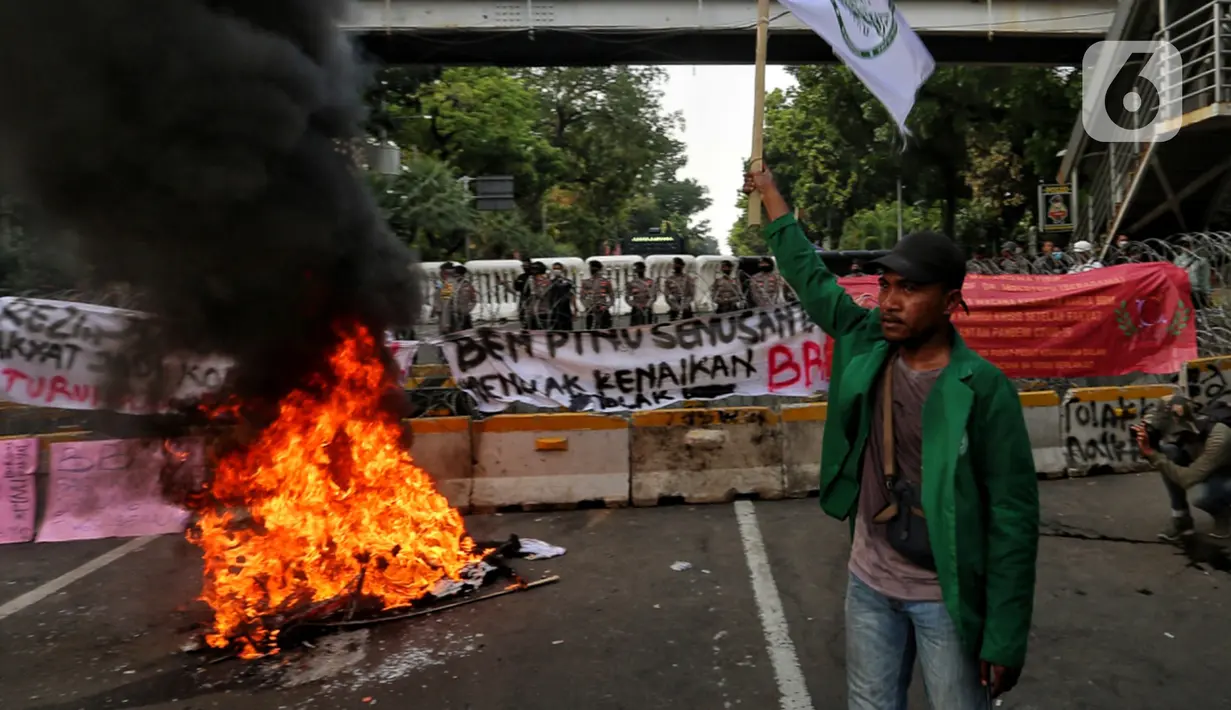 Seorang mahasiswa mengibarkan bendera saat sejumlah elemen mahasiswa menggelar demo dengan membakar ban bekas di kawasan Patung Kuda, Jakarta Pusat, Selasa (13/9/2022). Demo tersebut untuk menolak kebijakan pemerintah menaikkan harga bahan bakar minyak (BBM). (Liputan6.com/Johan Tallo)