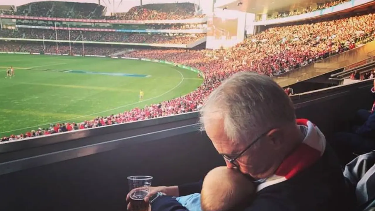 Perdana Menteri Australia, Malcom Turnbull, menonton pertandingan football sambil momong cucu dan membawa bir. (Foto: Facebook Malcolm Turnbull)