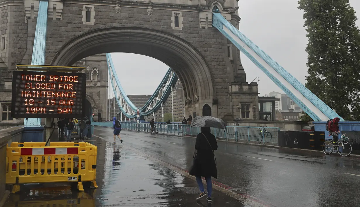 Orang-orang berjalan melewati papan tanda dekat Tower Bridge di Sungai Thames di London, Senin (9/8/2021). Tower Bridge London macet terbuka karena kesalahan teknis mengakibatkan gangguan lalu lintas di kedua sisi Sungai Thames karena mobil dan pejalan kaki tidak dapat menyeberang. (AP/Tony Hicks)