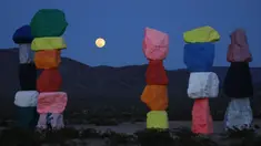 Supermoon terlihat dari celah instalasi seni Seven Magic Mountains karya seniman Ugo Rondinone di Las Vegas, Amerika Serikat, Selasa (7/4/2020). Seven Magic Mountains adalah instalasi seni tumpukan batu setinggi 35 kaki. (AP Photo/John Locher)