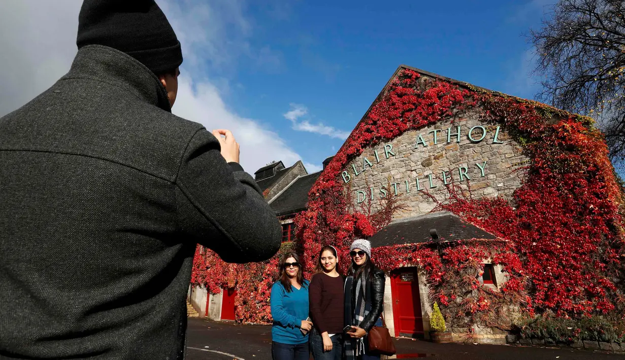 Wisatawan berpose di dekat Blair Athol Distillery, Skotlandia, Selasa (18/10). Blair Athol Distillery adalah kawasan objek wisata dengan bangunan unik karena ditumbuhi tumbuhan merambat berwarna merah.( REUTERS / Russell Cheyne)