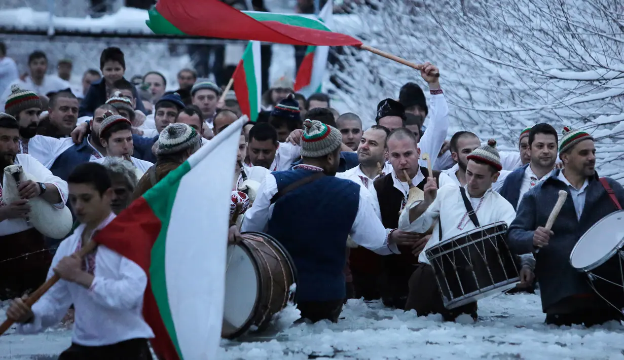 Sejumlah pria Bulgaria mengibarkan bendera sambil memainkan alat musik tradisional sambil menari di perairan sungai Tundzha selama Hari Epiphany di kota Kalofer, Bulgaria (6/1). (AP Photo/Valentina Petrova)