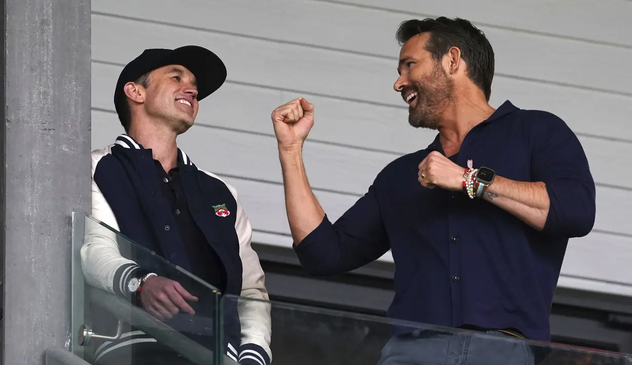 Aktor Hollywood, Ryan Reynolds (kanan) dan pemilik klub Wrexham, Rob McElhenney bercengkrama saat laga English National League antara Wrexham melawan Boreham Wood di Racecourse Ground Stadium, Wrexham, Wales, Sabtu (22/04/2023). Wrexham menang dengan skor 3-1 dan berhasil promosi ke Liga Dua Inggris. (AP/PA/Martin Rickett)