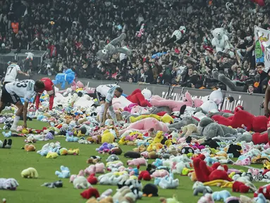 Pemain Besiktas dan Antalyaspor dibantu petugas mengumpulkan boneka yang dilemparkan oleh penonton pada laga lanjutan Liga Turki 2022/2023 yang berlangsung di Stadion Vodafone, Istanbul, Minggu (27/02/2023). Aksi tersebut ditujukan sebagai bentuk sumbangan untuk anak-anak korban gempa Turki. (AP Photo)