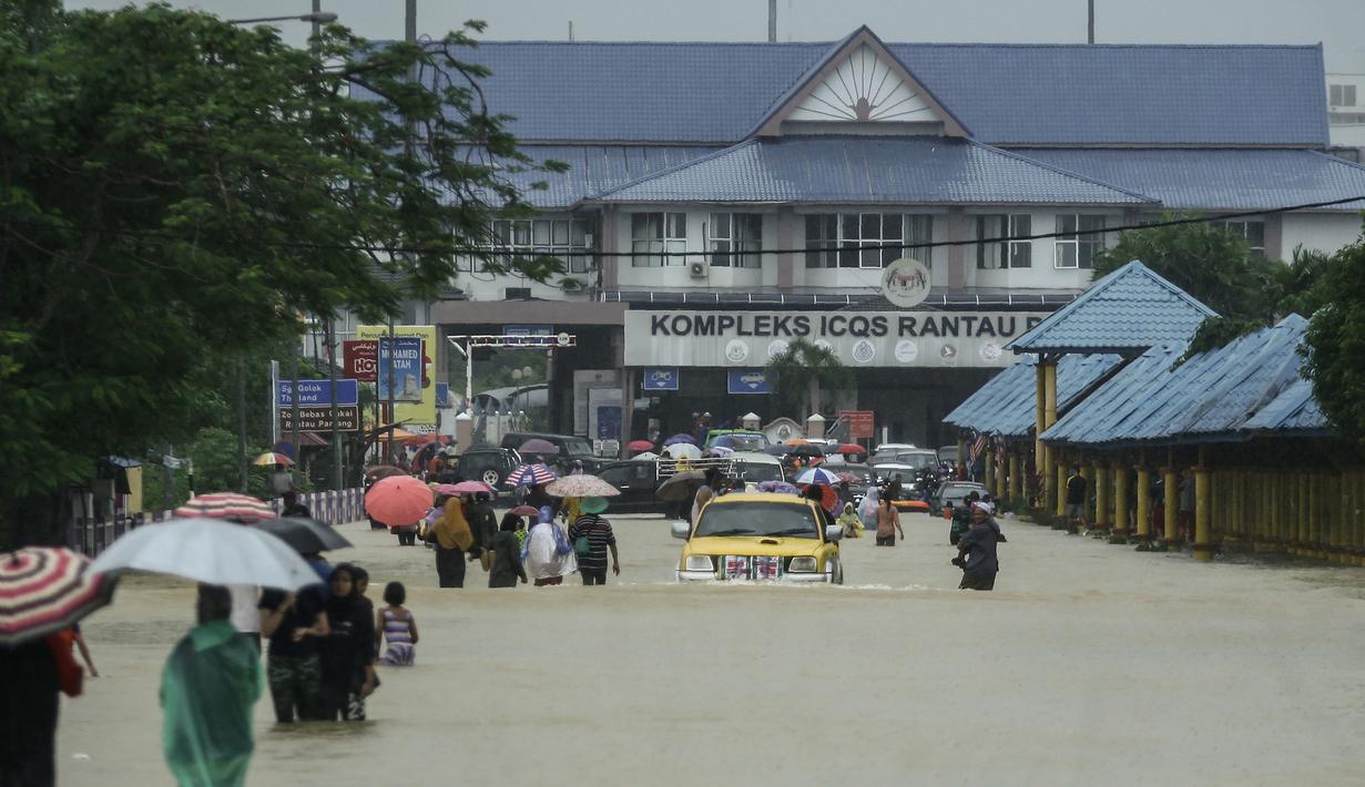 Warga menerobos banjir yang menggenangi jalanan di depan Kantor imigrasi dan bea cukai di Rantau Panjang, Selasa (3/1). Akibat hujan lebat yang turun terus menerus selama empat hari di Malaysia, 5000 warga terpaksa dievakuasi. (AFP PHOTO/STR/Malaysia OUT)