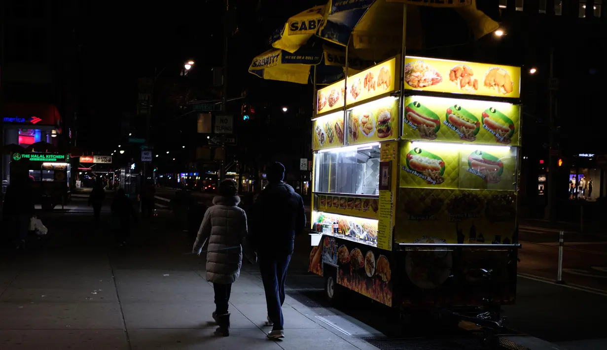 Pejalan kaki melewati gerobak makanan di New York, Senin (16/3/2020). Tiga wilayah juga akan membatasi kapasitas kerumunan untuk pertemuan sosial dan rekreasi hingga 50 orang. (AP Photo/Yuki Iwamura)