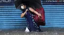 Seorang wanita mengenakan masker sebagai tindakan pencegahan terhadap virus corona melintasi banjir saat hujan lebat di Mumbai, India, Rabu, (5/8/2020). Musim hujan India berlangsung dari Juni hingga September. (AP Photo/Rajanish Kakade)