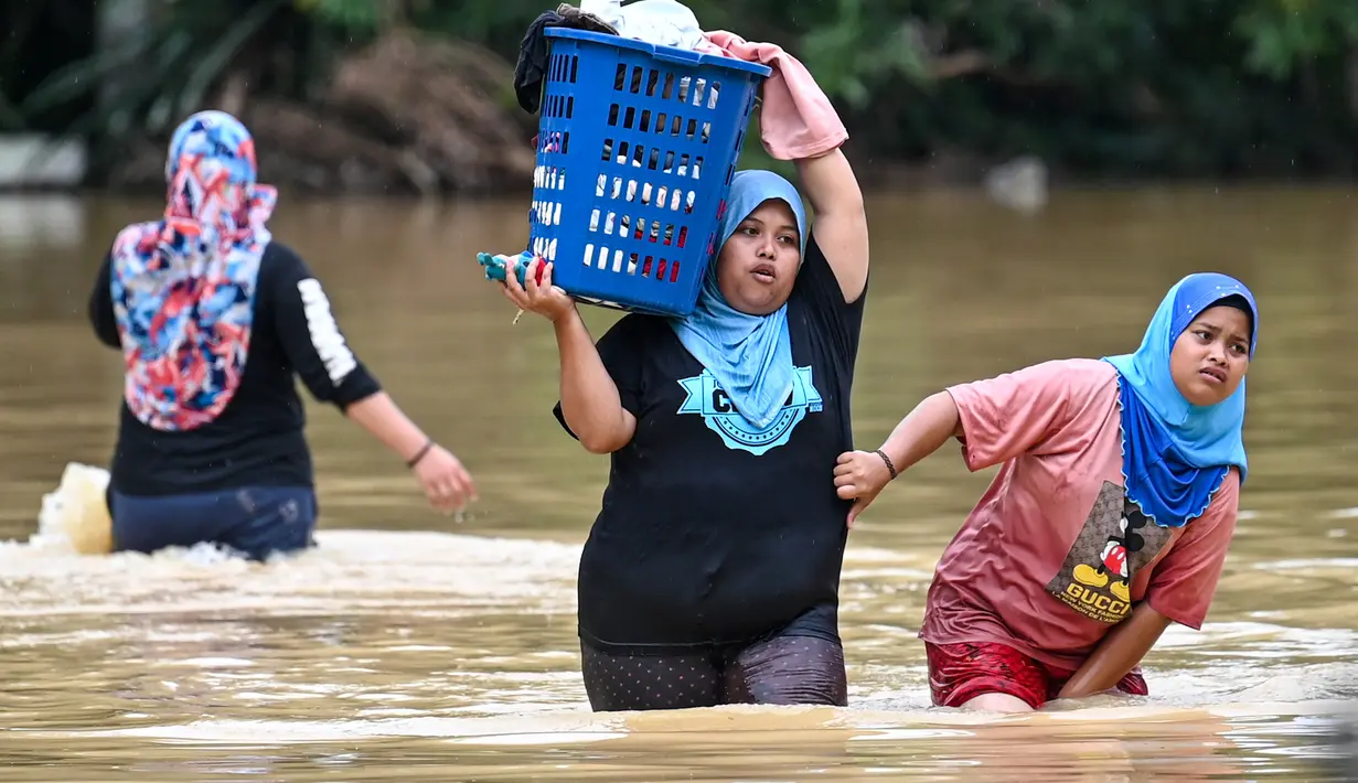 Warga membawa barang-barang mereka melalui air banjir di Kuala Kaung, dekat Lanchang di negara bagian Pahang Malaysia (4/1/2021).  Tiga sungai di negara bagian itu - Sungai Lepar, Sungai Lipis dan Sungai Lembing - telah melewati tingkat bahaya mereka pada hari Minggu. (AFP/Mohd Rasfan)
