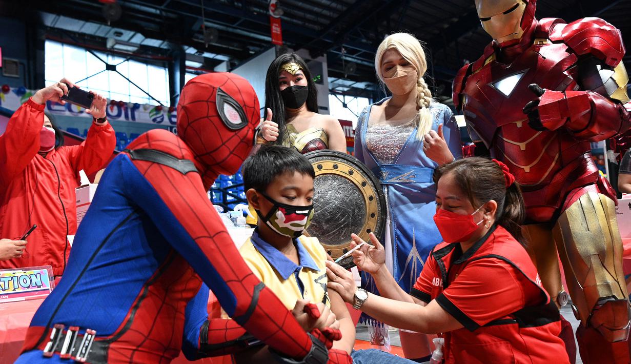 Dua orang berkostum superhero berpose dengan seorang anak yang menerima vaksin Covid-19 Pfizer-BioNtech untuk anak-anak berusia 5-11 di sebuah gym di San Juan City, pinggiran kota Manila, Filipina pada 7 Februari 2022. (Ted ALJIBE / AFP)