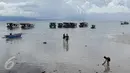 Sepasang wisatawan berjalan menuju kapal penumpang sementara seorang anak (kanan) bermain di pinggir pantai Pulau Bunaken, Manado, Sabtu (17/12). Taman Nasional Bunaken ini memiliki keindahan alam dan biota laut. (Liputan6.com/Fery Pradolo)