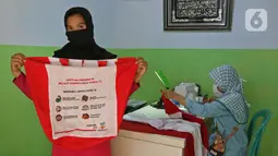 Warga menunjukkan tas sembako bantuan Presiden Joko Widodo di Jalan Caringin, Bedahan Barat, Sawangan, Depok, Jawa Barat, Jumat (7/8/2020). Bahan tas sembako berwarna merah putih tersebut dipasang sepanjang jalan Caringin untuk menyambut HUT ke-75 RI. (Liputan6.com/Herman Zakharia)