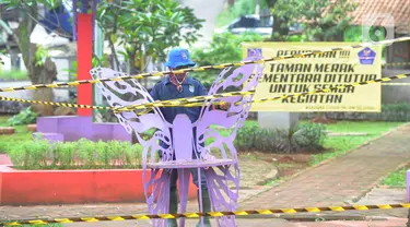 Petugas Dinas Lingkungan Hidup dan Kebersihan (DLHK) Kota Depok memasang garis larangan melintas umum di Taman Merak, Limo, Depok, Senin (25/1/2021). Pembatasan dan penutupan taman tersebut dilakukan dalam rangka Pemberlakuan Pembatasan Kegiatan Masyarakat (PPKM). (merdeka.com/Arie Basuki)