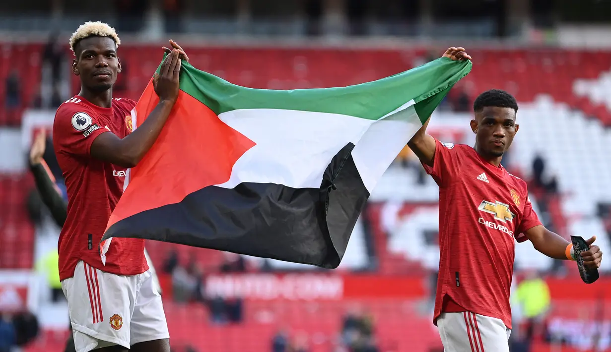 Penggawa MU, Paul Pogba dan Amad Diallo mengibarkan bendera Palestina usai ditahan imbang Fulham pada lanjutan Liga Inggris di Stadion Old Trafford, Rabu (19/5/2021) dinihari. Pogba dan Diallo menunjukkan solidaritas bagi Palestina yang tengah berseteru dengan Israel. (Laurence Griffiths/POOL/AFP)