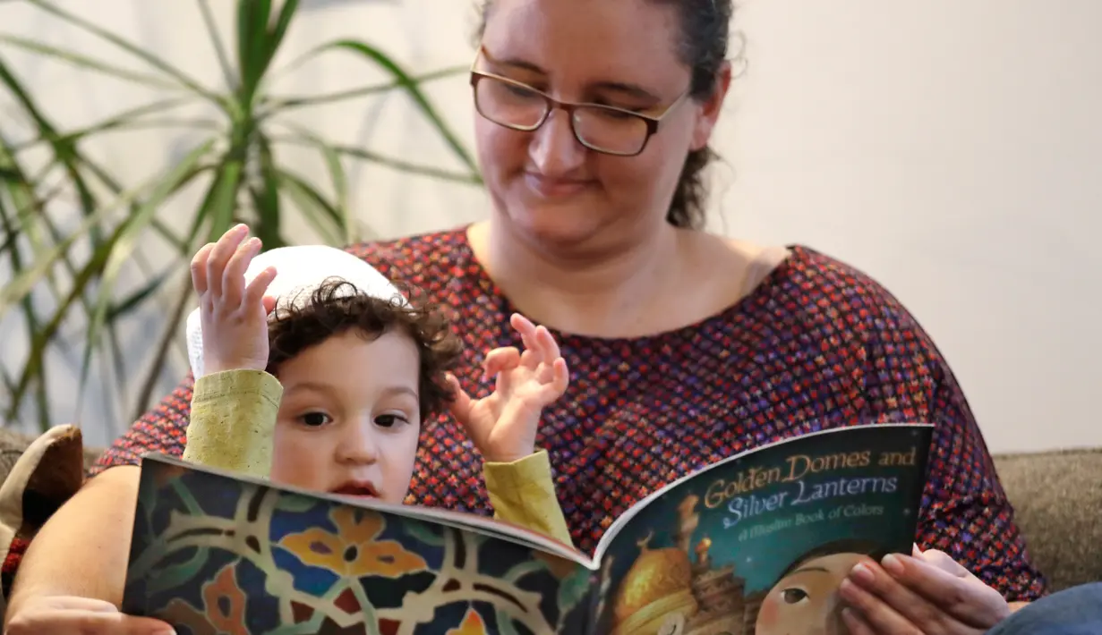 Yusuf Kamel (2) dibacakan buku ibunya, Nadia Chaouch  sambil menunggu buka puasa dirumahnya di Seattle (28/4/2020). Keluarga itu, seperti Muslim lainnya selama pandemi, melaksanakan bulan puasa Ramadan dengan doa dan refleksi dirumahnya daripada bertemu komunitas dan ke masjid. (AP/Elaine Thompson)