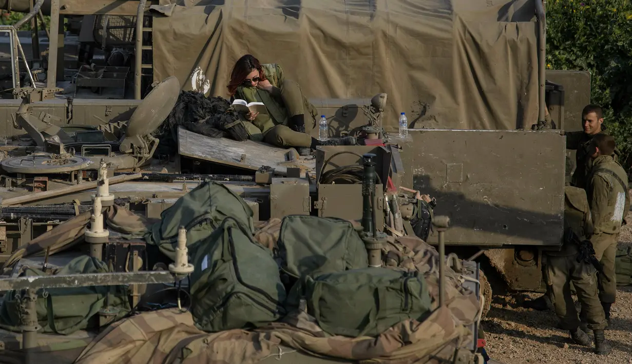 Tentara Israel membaca buku di atas artileri di dekat perbatasan dengan Gaza, Rabu (27/3). Brigade Infanteri dan Batalion Artileri tambahan dikerahkan untuk membantu pasukan militer Israel di sekitar perbatasan Gaza. (AP Photo/Tsafrir Abayov)