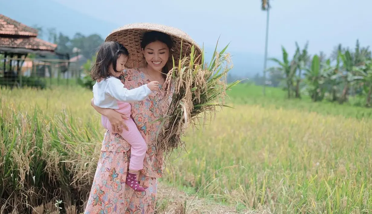 "Panen padi di sawah sendiri, sambil ngajarin Alia ini padi ya, kalau yg Alia makan udh jadi nasi, hahaha😍😍," tulisnya sebagai keterangan foto sambil mengendong putrinya. (Instagram/sarwendah29)