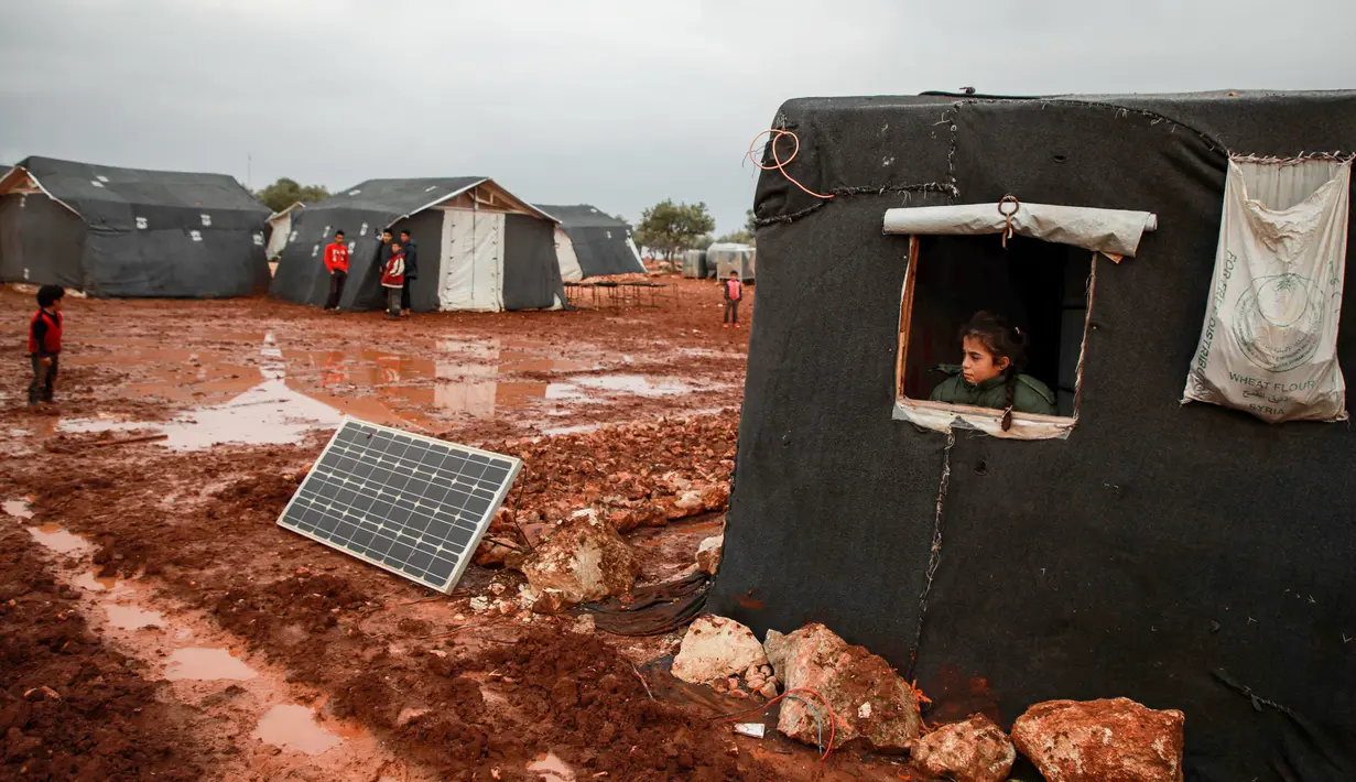 Seorang gadis melihat ke luar jendela sebuah tenda di sebuah kamp untuk warga Suriah yang kebanjiran di dekat desa Killi di utara provinsi Idlib barat laut (5/12/2019). (AFP Photo/Aaref Watad)