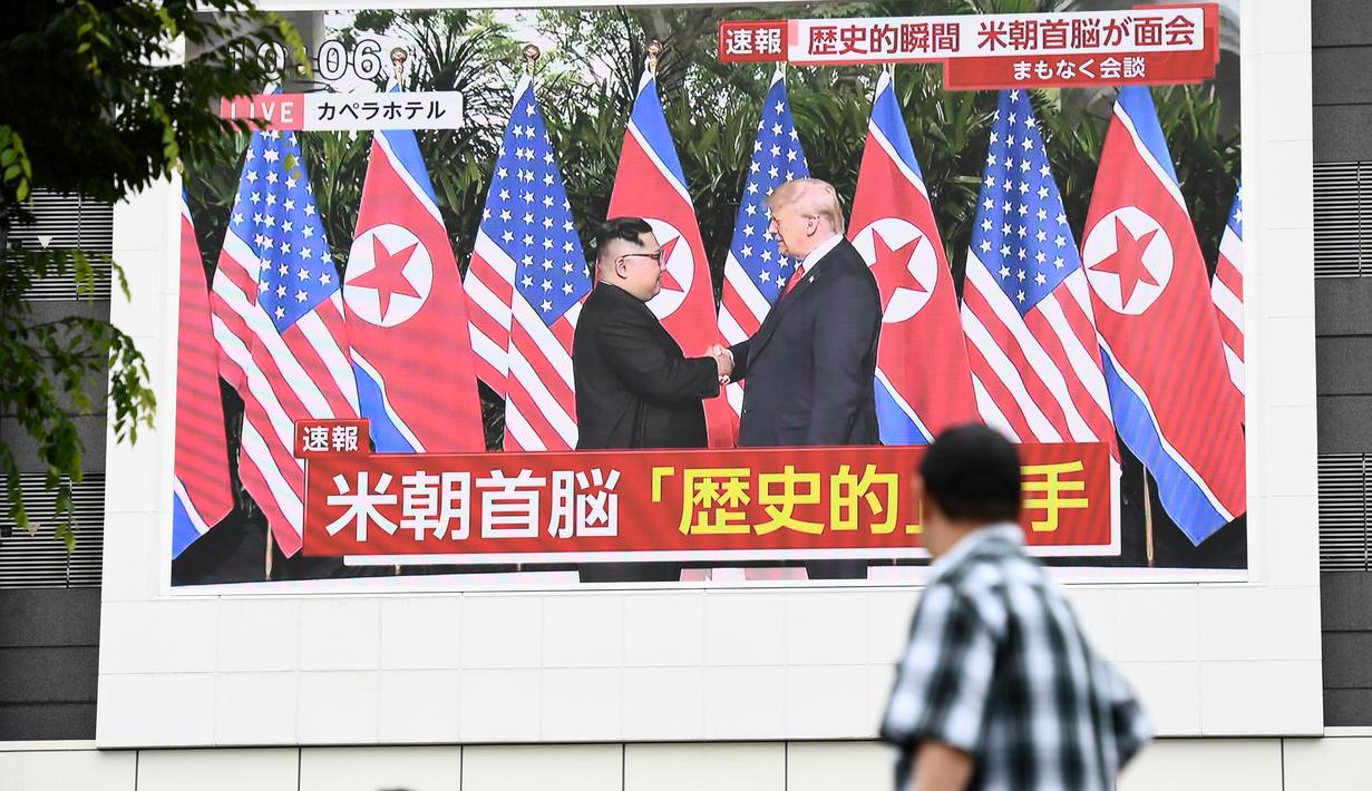 Pejalan kaki melihat layar yang menampilkan pertemuan antara pemimpin Korea Utara Kim Jong-un dan Presiden AS Donald Trump di Tokyo, Selasa (12/6). Untuk pertama kalinya dalam sejarah, Donald Trump dan Kim Jong-un bertemu. (AFP PHOTO/Martin BUREAU)
