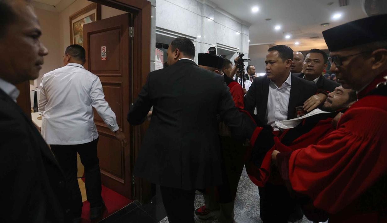 Anwar Usman kemudian dibopong menuju ruang tunggu Mahkamah Konstitusi untuk mendapatkan penanganan medis dari tim dokter. Tampak dalam foto, Anwar Usman dibopong ke ruang tunggu usai mengikuti prosesi wisuda purnabakti di Ruang Sidang Mahkamah Konstitusi (MK), Jakarta, Senin (13/4/2026). (Kapanlagi.com/Budy Santoso)