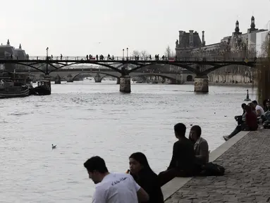 Orang-orang duduk di tepi sungai Seine di Paris, Rabu (3/3/2021).  Tingkat infeksi COVID-19 tetap tinggi selama beberapa minggu, dan pasien virus menempati 70% unit perawatan intensif negara itu. (AP Photo/Lewis Joly)