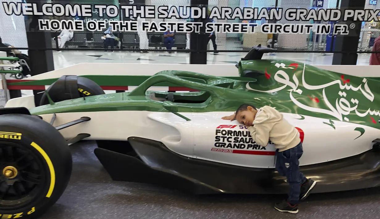 Seorang anak memeluk mobil balap yang mempromosikan Formula One (F1), di Bandara Internasional King Abdulaziz di Jeddah, Arab Saudi, Selasa (30/11/2021). Arab Saudi untuk pertama kalinya dipercaya menjadi tuan rumah balapan F1 2021, yang akan berlangsung 3-5 Desember mendatang. (AP Photo/Amr Nabil)