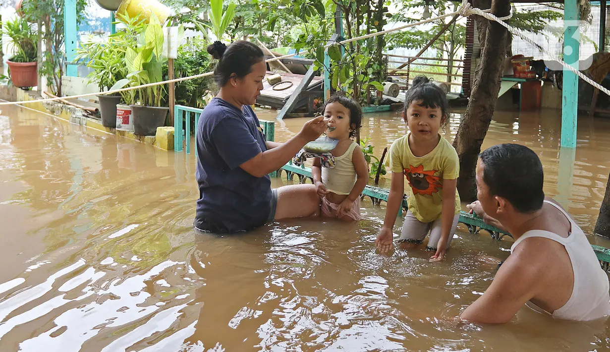 Seorang ibu menyuapi anaknya makan di tengah banjir yang melanda kawasan Cipinang Melayu, Jakarta Timur, Jumat (19/2/2021). Banjir di kawasan tersebut akibat curah hujan yang tinggi dan meluapnya air dari Kali Sunter. (Liputan6.com/Herman Zakharia)