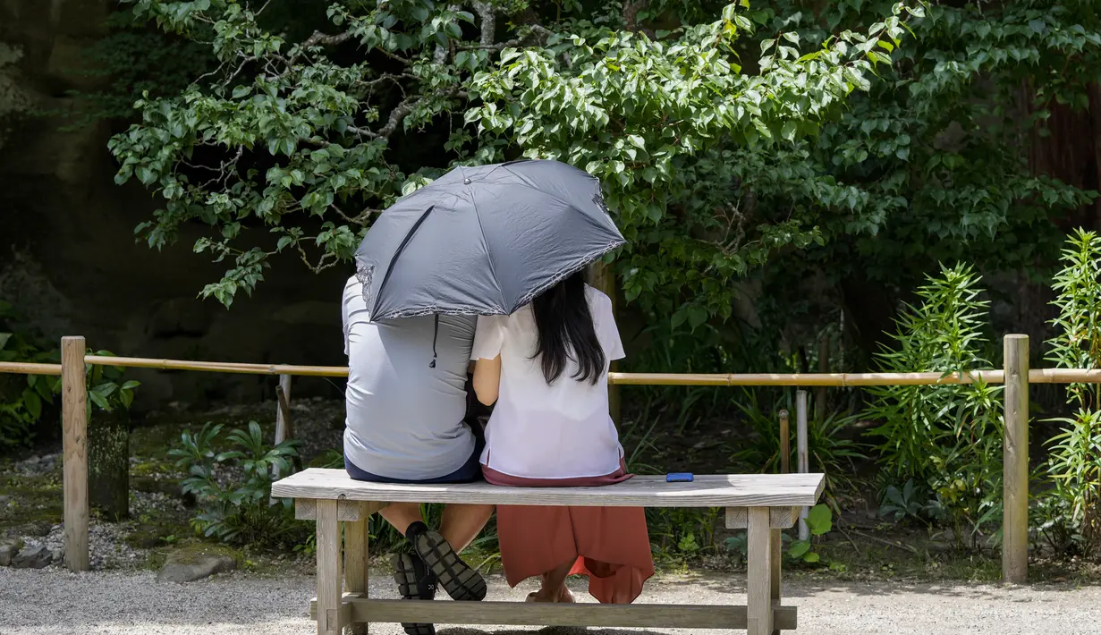 Sepasang kekasih duduk menggunakan payung agar terhindar dari sinar matahari saat mereka berada di kuil Buddha Meigetsu-in di Kamakura, Tokyo, Jepang, Jumat (11/6/2021).  (AP Photo/Kiichiro Sato)
