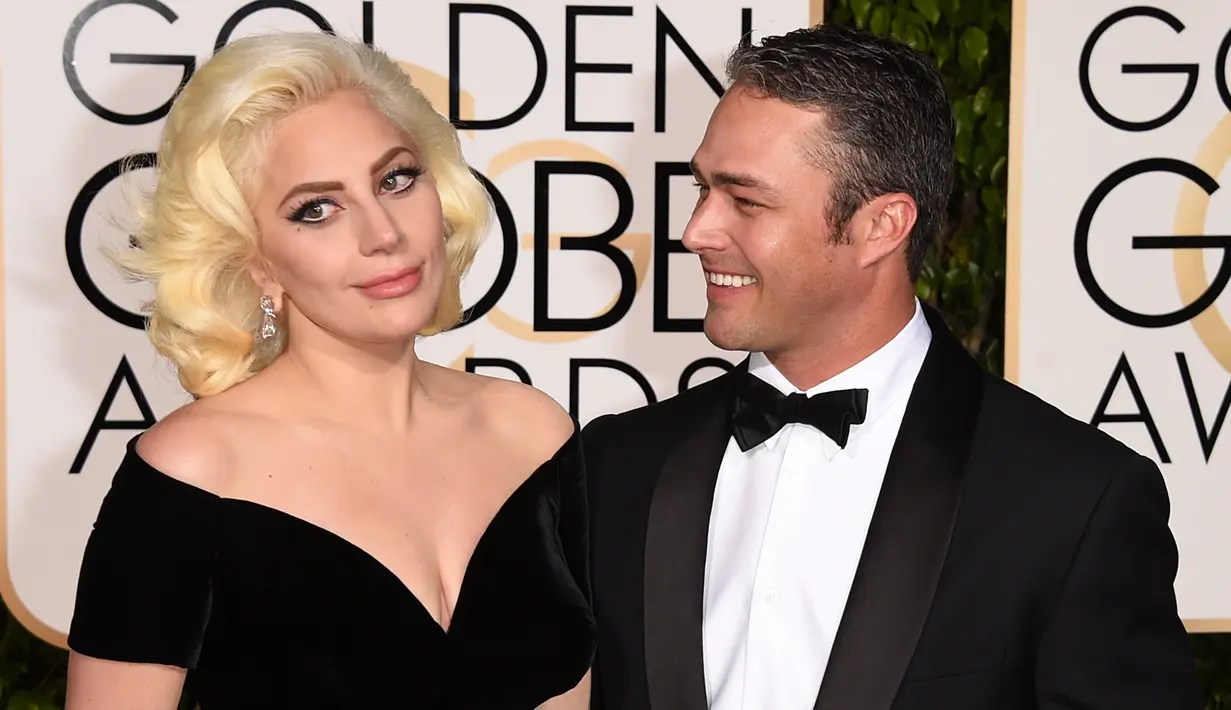 Lady Gaga ditemani Taylor Kinney menghadiri acara Golden Globes 2016 di Beverly Hilton Hotel, California, Minggu (10/1). Kompak mengenakan gaun bernuansa hitam, sang Mother Monster menggandeng mesra sang tunangan. (Jason Merritt/Getty Images/AFP)