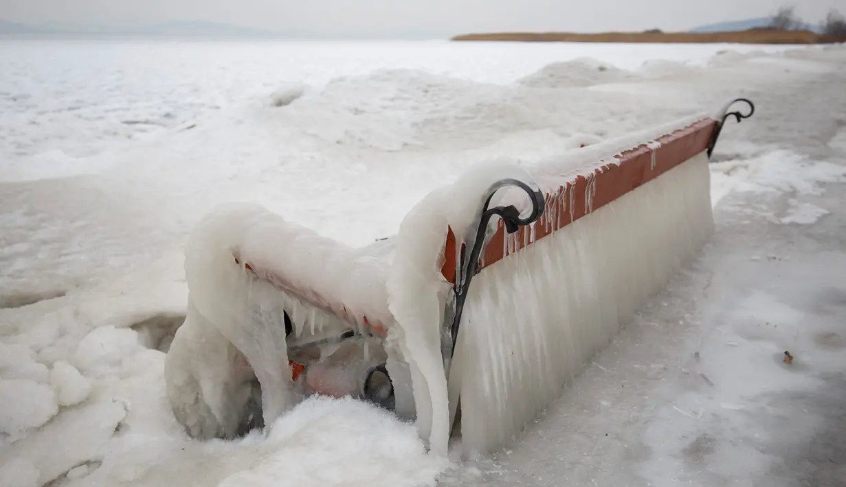 Sebuah bangku tertutup salju di tepi Danau Balaton di Balatonfenyves, Hungaria (26/2). Karena cuaca ekstrem tersebut banyak bangunan dan tempat yang beku tertutup salju. (Gyorgy Varga / MTI via AP)