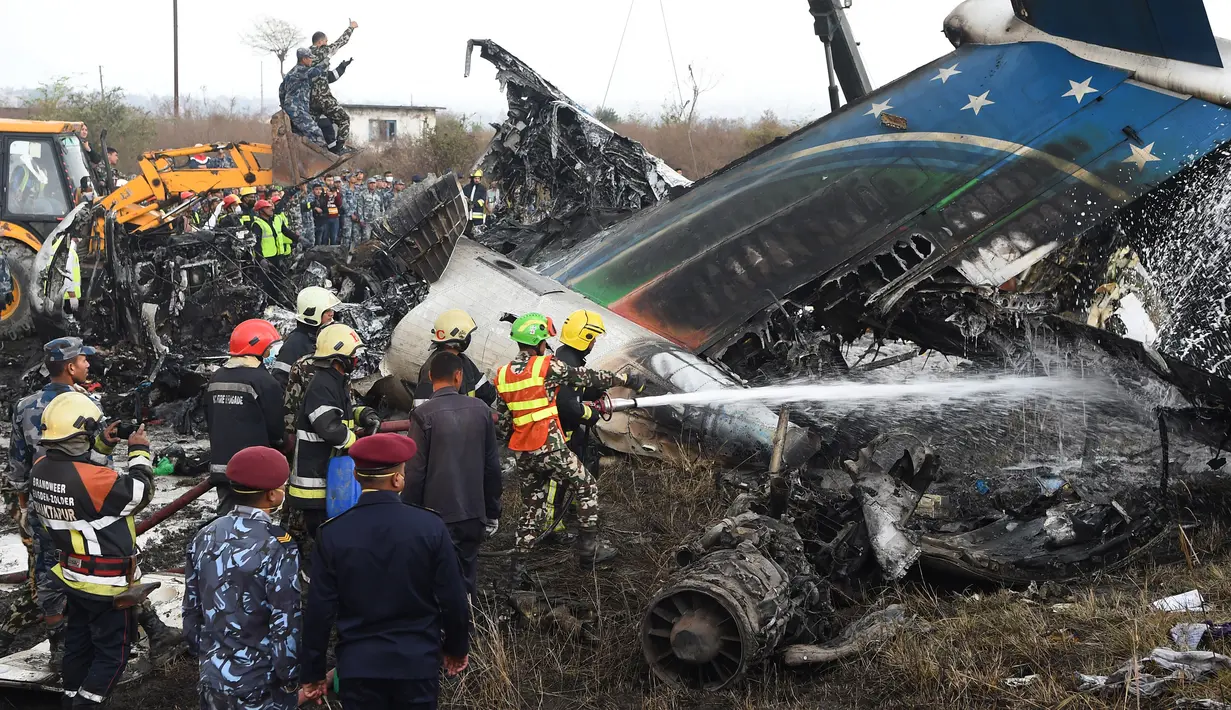 Tim penyelamat berusaha memadamkan api pada puing pesawat yang jatuh di dekat Bandara Internasional Kathmandu, Nepal, Senin (12/3). Pejabat setempat mengatakan ada 71 orang di dalam pesawat tersebut. (Prakash MATHEMA/AFP)