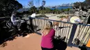 Keluarga mengunjungi kandang jerapah di Kebun Binatang Taronga di Sydney (18/10/2021). Kebun binatang Taronga membuka kembali pintunya bagi pengunjung yang divaksinasi setelah pencabutan pembatasan penguncian Sydney. (AFP/Saeed Khan)