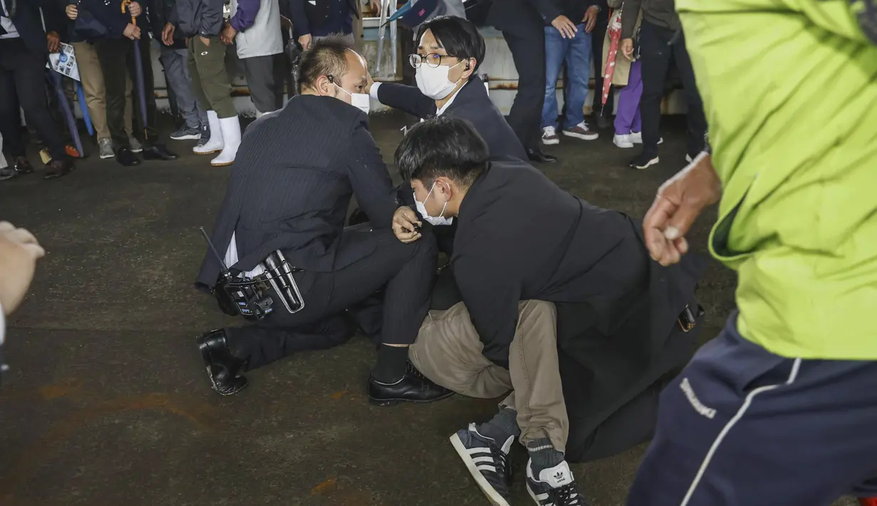 Seorang pria (di tanah) yang melemparkan apa yang tampak seperti bom asap, ditangkap di sebuah pelabuhan di Wakayama, Jepang barat, Sabtu (15/4/2023). (Kyodo News via AP)