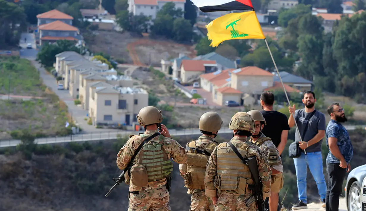 Tentara Lebanon berdiri di sebuah bukit yang menghadap ke Kota Metula di Israel ketika seorang pria mengibarkan bendera Palestina dan Hizbullah di sisi perbatasan Lebanon-Israel di desa selatan Kfar Kila, Lebanon, Senin (9/10/2023). Pasukan Israel menembak dan membunuh beberapa pria bersenjata yang menyeberang ke negara itu dari Lebanon, kata Pasukan Pertahanan Israel tanpa menyebutkan jumlah orang yang terbunuh atau dugaan afiliasi mereka. (AP Photo/Mohammed Zaatari)