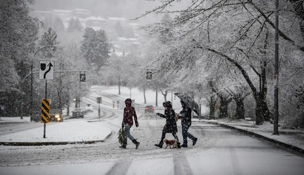 Warga berjalan saat hujan salju yang cukup lebat di Burnaby, British Columbia, Kanada (21/12/2020). Pemerintah setempat mengeluarkan peringatan hujan salju pada hari pertama musim dingin. (Darryl Dyck/The Canadian Press via AP)