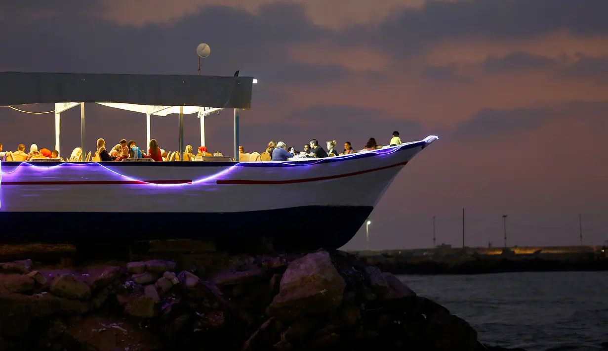 Pengunjung menikmati hidangan pada senja hari di sebuah restoran berbentuk perahu, tepi pantai Kota Gaza, Jalur Gaza, Rabu (2/8). Di restoran unik itu, pengunjung bisa menikmati lezatnya makanan sambil melihat matahari tenggelam. (MOHAMMED ABED / AFP)
