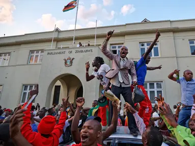 Warga Zimbabwe bergembira setelah kabar Presiden Robert Mugabe mengundurkan diri di luar gedung parlemen, pusat kota Harare, Selasa (21/11). Surat pengunduran diri Robert Mugabe itu mengakhiri masa pemerintahannya selama 37 tahun. (AP/Ben Curtis)