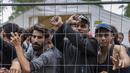 Para migran berdiri di belakang pagar di dalam kamp pengungsi yang baru dibangun di tempat latihan militer Rudninkai, sekitar 38km (23,6 mil) selatan dari Vilnius, Lituania, Rabu (4/8/2021). (AP Photo/Mindaugas Kulbis)
