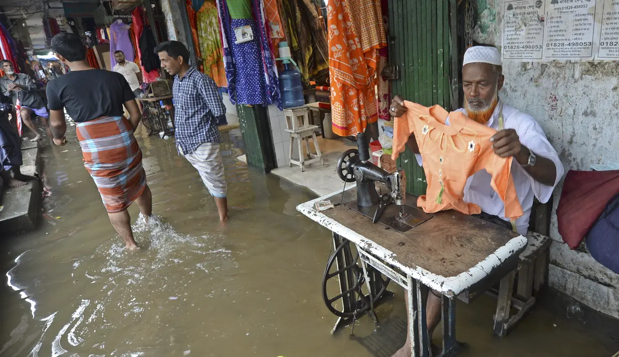 Seorang penjahit bekerja di luar sebuah toko di sebuah pusat perbelanjaan yang tergenang air setelah hujan lebat di Dhaka (21/7/2020). Korban tewas akibat hujan lebat di Asia Selatan telah meningkat menjadi hampir 200. (AFP/Munir Uz zaman)