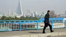 Seorang pria berjalan di jembatan dengan latar Ryugyong Hotel berbentuk piramida terlihat di Pyongyang, Korea Utara, (21/10). (AP Photo / Dita Alangkara)