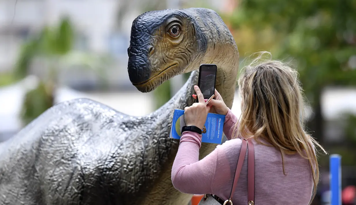 Seorang wanita mengambil foto replika dinosaurus Europasaurus seukuran aslinya di pusat kota Bochum, Jerman (12/8/2019). Jejak dinosaurus berumur 316 juta tahun ditemukan di lubang batu di kota itu enam tahun lalu di kota ini. (AP Photo/Martin Meissner)